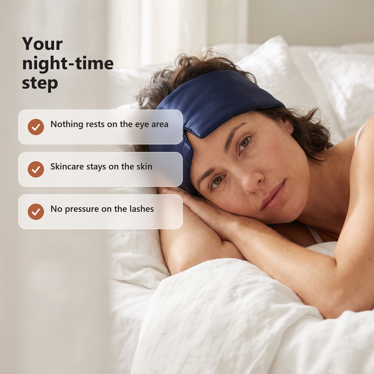 A woman resting on white bedding with the mask pushed up on her forehead, beside three benefit cards