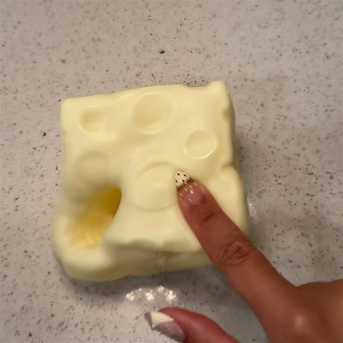 A finger pressing into the yellow CHEDDI cheese squishy