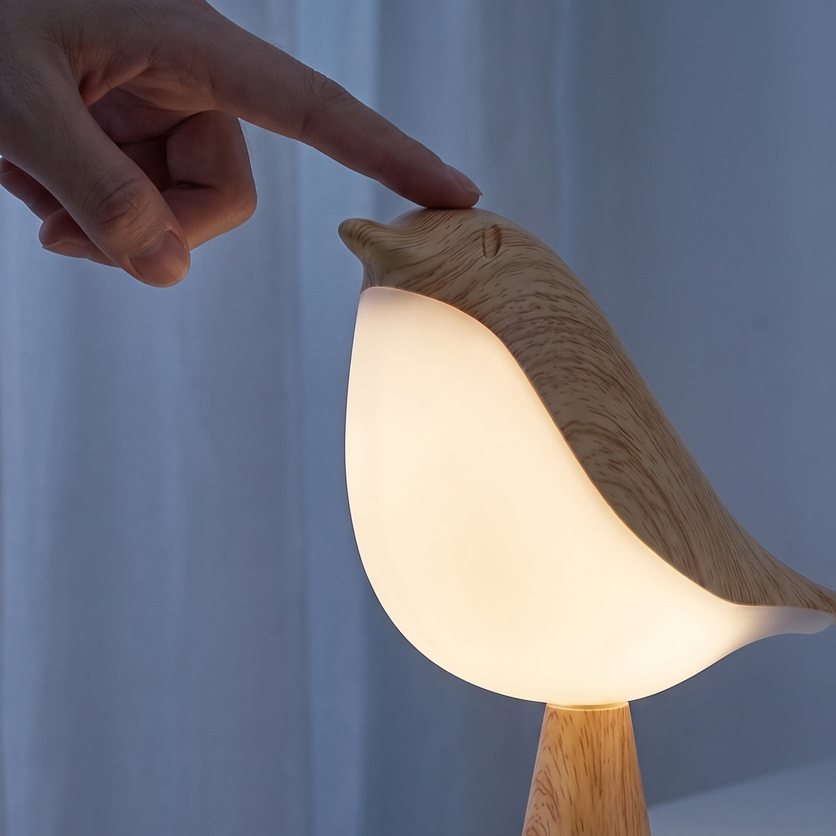 A fingertip touching the wooden head of the Songlow bird lamp to switch it on